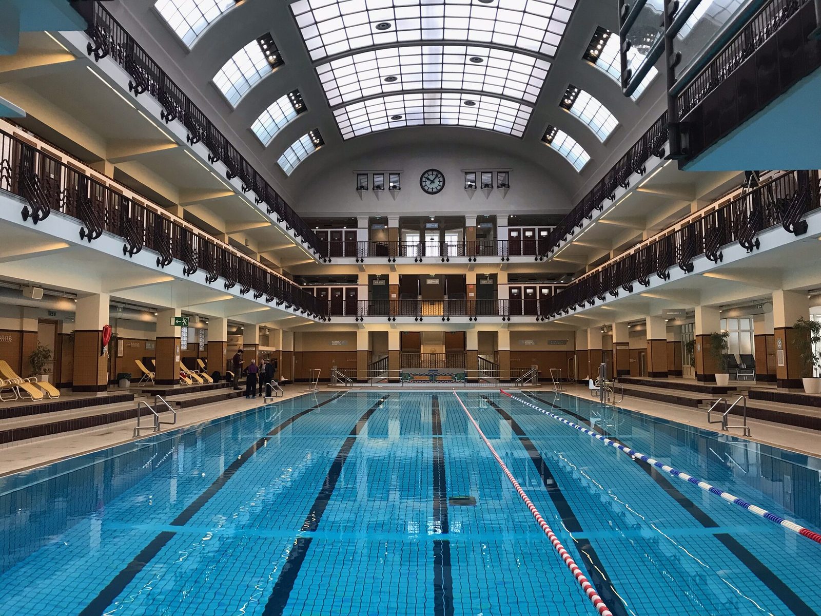 Wnętrze Amalienbad w Wiedniu — główna hala basenowa z galeriami, drewnianymi balustradami i szklanym świetlikiem nad 33,5-metrowym basenem